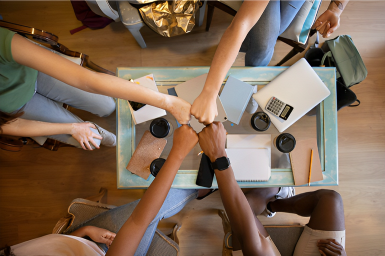 Mãos de várias pessoas unidas com as palmas fechadas sobre uma mesa de escritório, simbolizando a cultura empresarial.